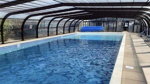 Una piscina con techo de vidrio, rodeada por un solárium empedrado.