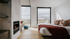 Een slaapkamer met een bed, een open haard, een groot raam en uitzicht op het landschap.