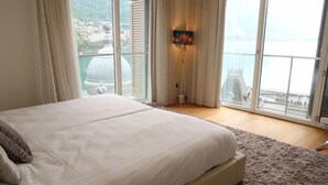 A bedroom with a large bed, a view of a cityscape through floor-to-ceiling windows, and a decorative wall light. - L'Esplanade A3.8 by Interhome (Montreux)