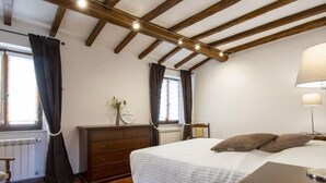 A bedroom with a wooden ceiling, a bed with white bedding, a dresser, a nightstand, and a lamp. - Vacation home Kenzo by Interhome (Bagni di Lucca)