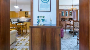 Un vaste espace de vie comprenant un salon avec une table basse en bois, une table à manger avec des chaises, une cuisine avec des meubles en bois et un lustre.