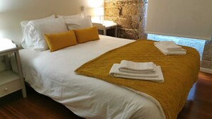 A neatly made bed with white and mustard bedding, a folded white towel, and a stone wall in the background. - Villa em Arcos de Valdevez - Quinta com piscina privada , adequado para familias (Gondoriz - Arcos de Valdevez)