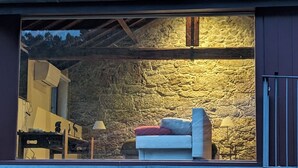 A cozy room with a stone wall, a white sofa with a red cushion, and a small table with a lamp. - Villa em Arcos de Valdevez - Quinta com piscina privada , adequado para familias (Gondoriz - Arcos de Valdevez)