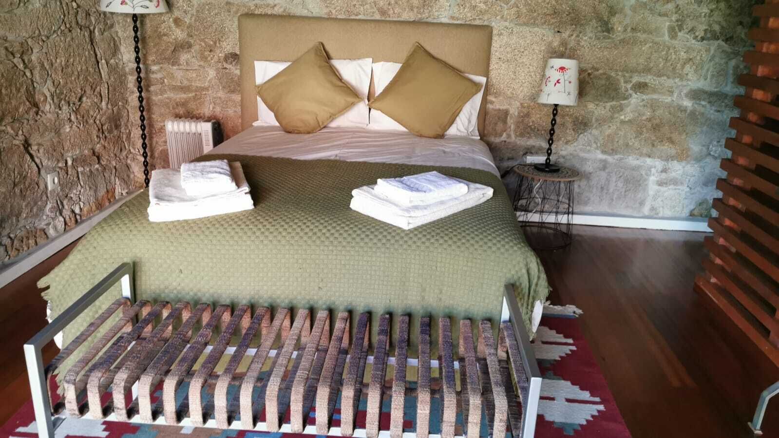 A bed with a headboard, pillows, and a blanket. There is a small table with a lamp beside the bed.