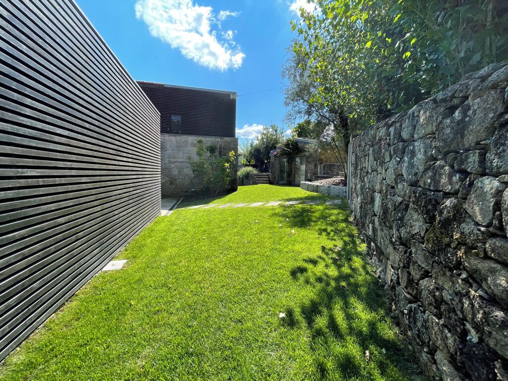 Un edificio moderno con techo inclinado, pared de piedra y césped cuidado.