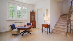 A spacious living room with a large window, a wooden cabinet, a round table, and a staircase. - Villa Clara by Interhome (Lido di Camaiore)