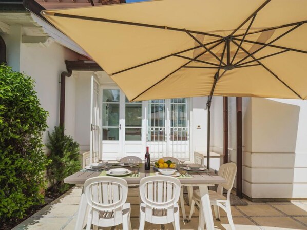 An outdoor dining area with a table set for two, a yellow umbrella, and a bottle of wine.