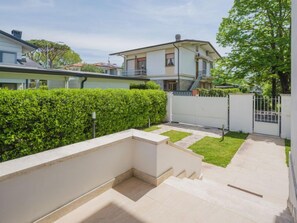 Un quartier résidentiel moderne doté d’un jardin bien entretenu, d’un chemin pavé et d’une entrée sécurisée par un portail.