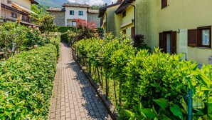 A narrow cobblestone path flanked by lush greenery and traditional buildings with balconies and wooden shutters. - La Perla by Interhome (Colico)