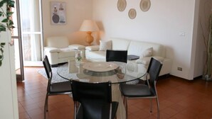 Een moderne woonkamer met een glazen eettafel, omringd door stoelen, een witte bank en een lamp.