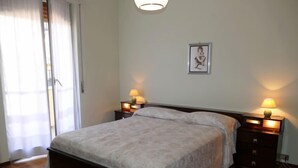Une chambre à coucher bien rangée, avec un grand lit, deux tables de chevet avec des lampes, un tableau encadré au mur et une porte-fenêtre coulissante.