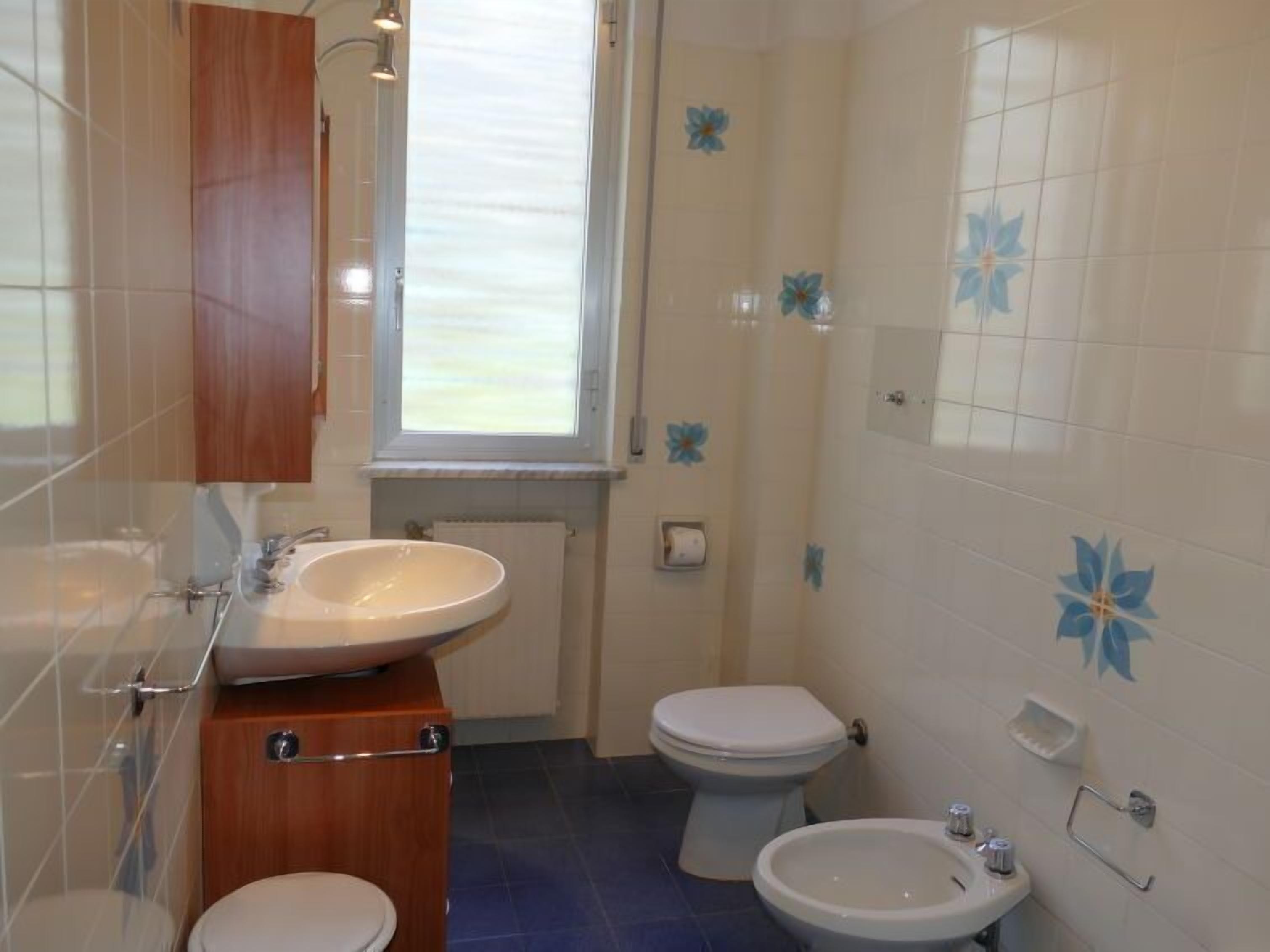 A bathroom with a wooden vanity, a sink, a toilet, and a bidet.