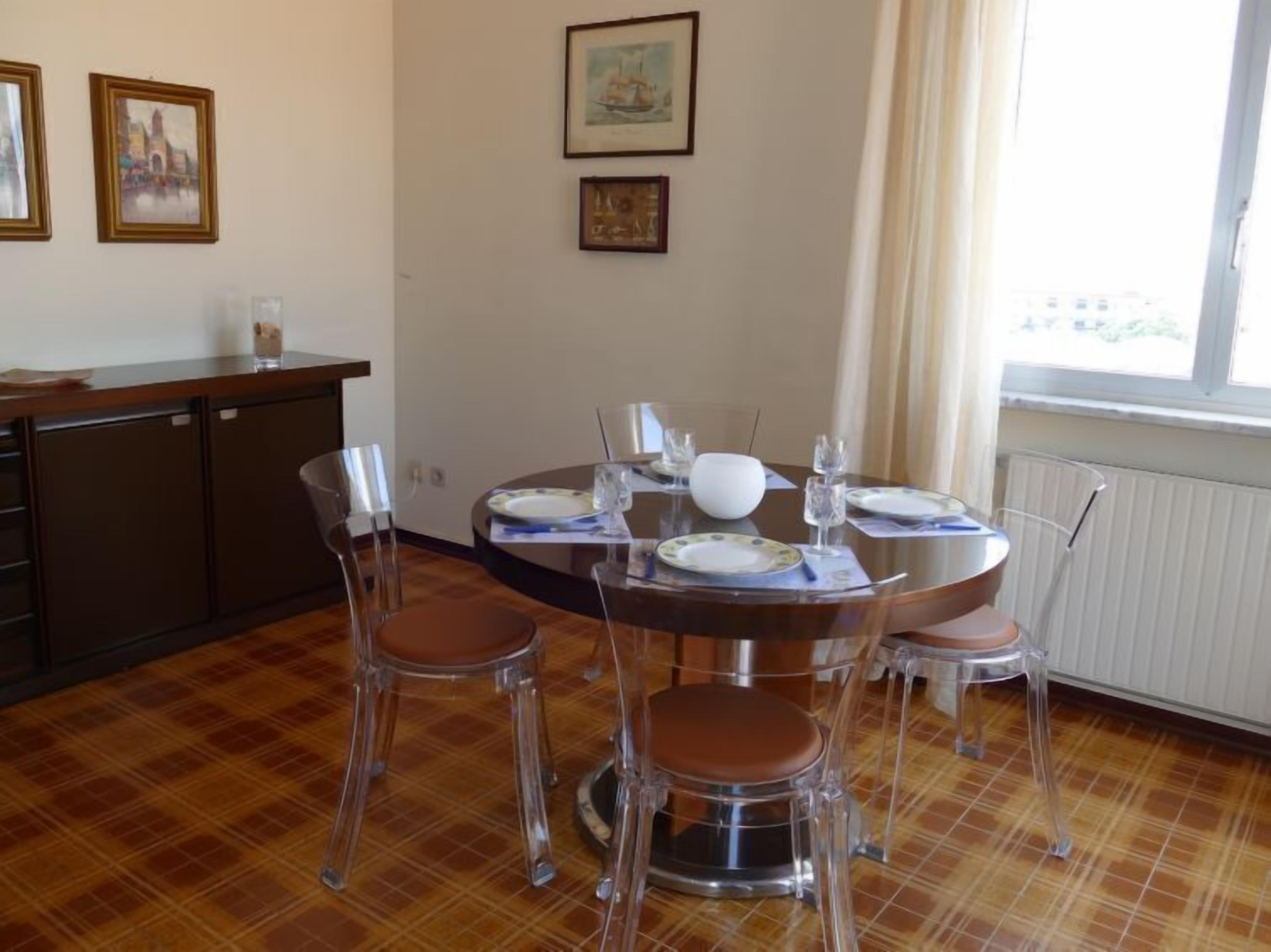 Un comedor con una mesa redonda, sillas de plástico transparente y un armario de madera.