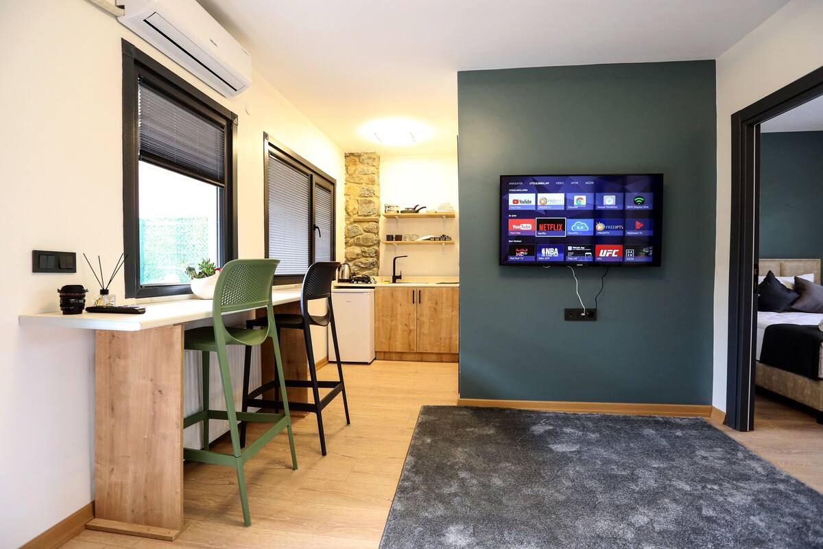 A modern kitchen with a stone accent wall, a wooden dining table, and a TV displaying various streaming services.