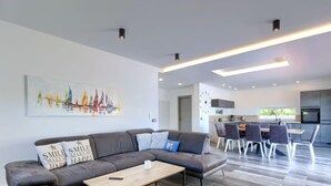 Uma sala de estar moderna com um sofá seccional, uma mesa de centro e uma área de jantar, com uma cozinha ao fundo.