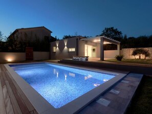 Ett modernt hus med en swimmingpool, en täckt uteplats och en mur av sten.