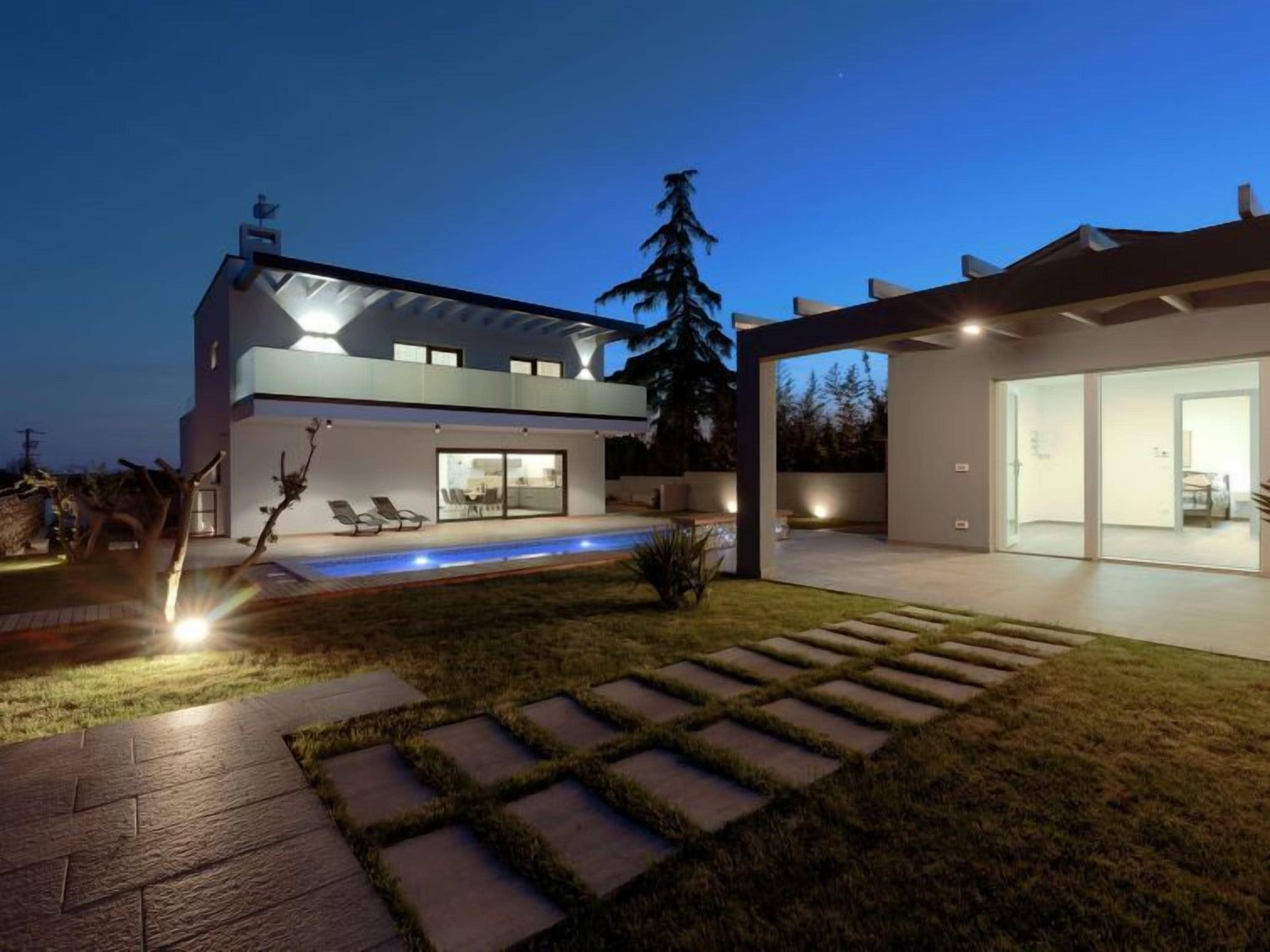 Ein modernes, zweigeschossiges Haus mit Swimmingpool, überdachter Terrasse und gepflegtem Rasen.