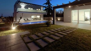 Uma casa moderna de dois andares com piscina, varanda coberta e gramado bem cuidado.