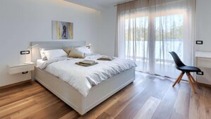 Quarto moderno com uma cama grande, mesas de cabeceira, escrivaninha e uma cadeira.