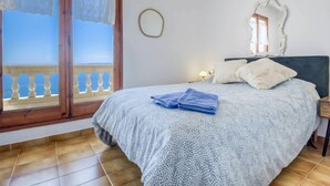 A bedroom with a bed, a nightstand, a mirror, and a view of the sea through a balcony. - Vacation home Bramer by Interhome (Roses)