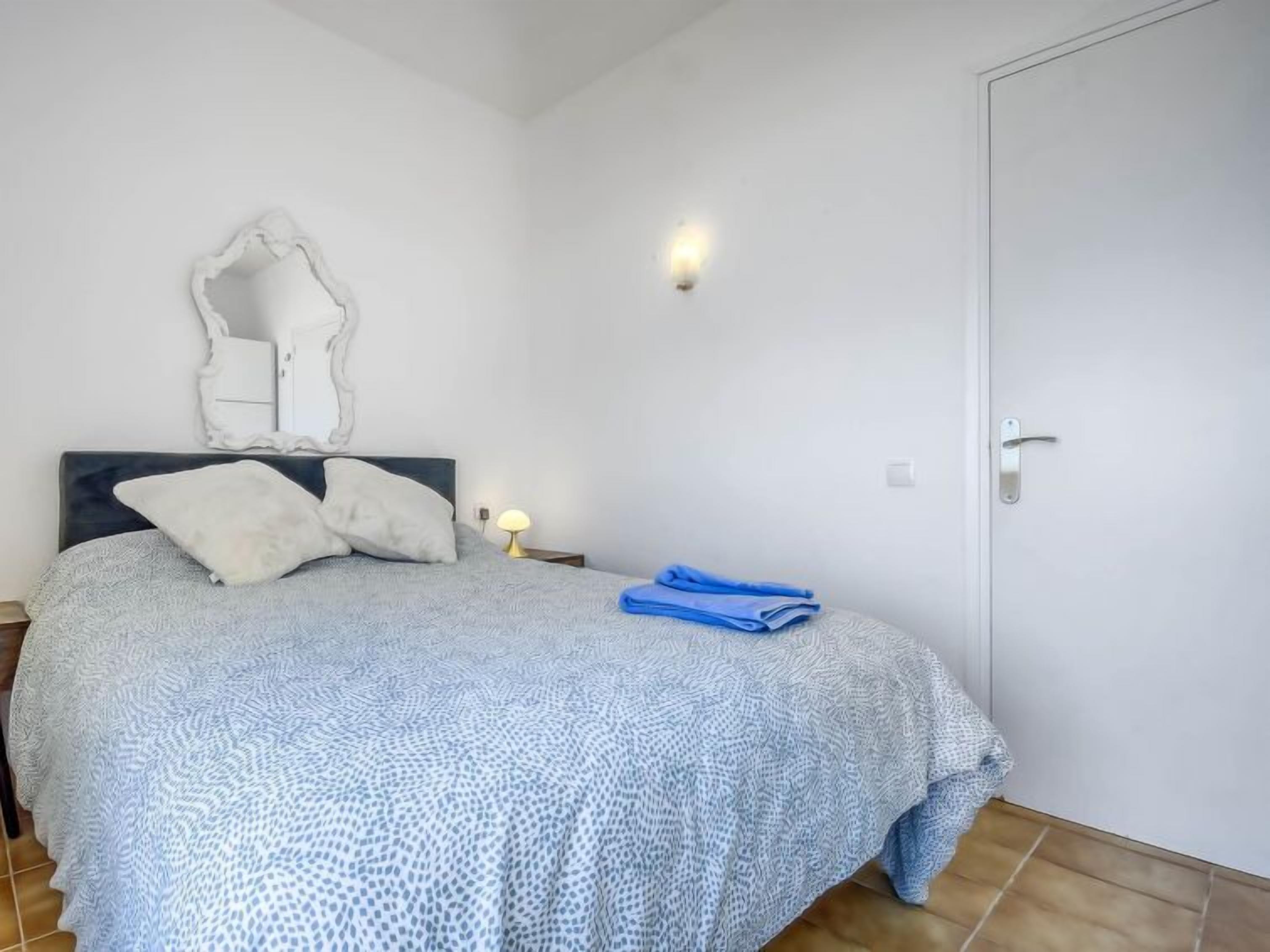 A bedroom with a bed, pillows, a nightstand, a lamp, and a door.