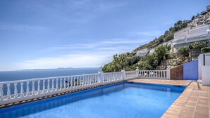 A swimming pool with a white balustrade, a clear view of the sea, and a hillside with buildings. - Vacation home Bramer by Interhome (Roses)