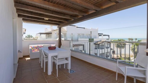 Un balcon avec une table et des chaises blanches, une vue sur la mer et un sol carrelé.