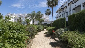Un chemin mène à un bâtiment moderne doté de balcons, entouré d’une végétation luxuriante et de palmiers.