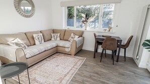 Una sala de estar moderna con un sofá seccional, una mesa de comedor con sillas, una pequeña alfombra y un espejo decorativo en la pared.