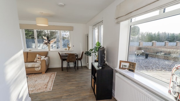 Una sala de estar moderna con un sofá, una mesa de comedor y sillas. Hay un ventanal con vistas a un jardín y un radiador blanco.