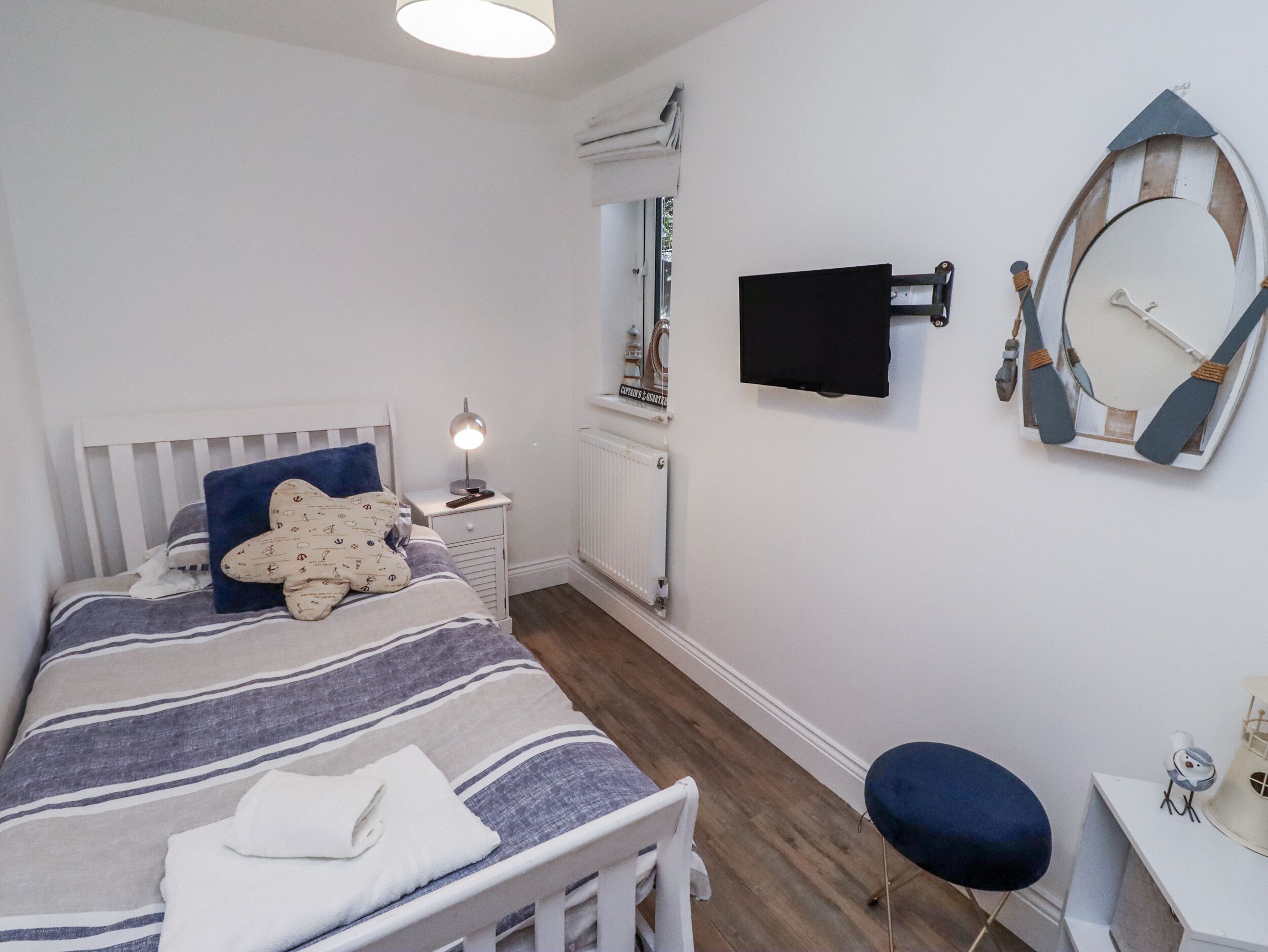 Un dormitorio con cama, mesita de noche, lámpara y televisor instalado en la pared.