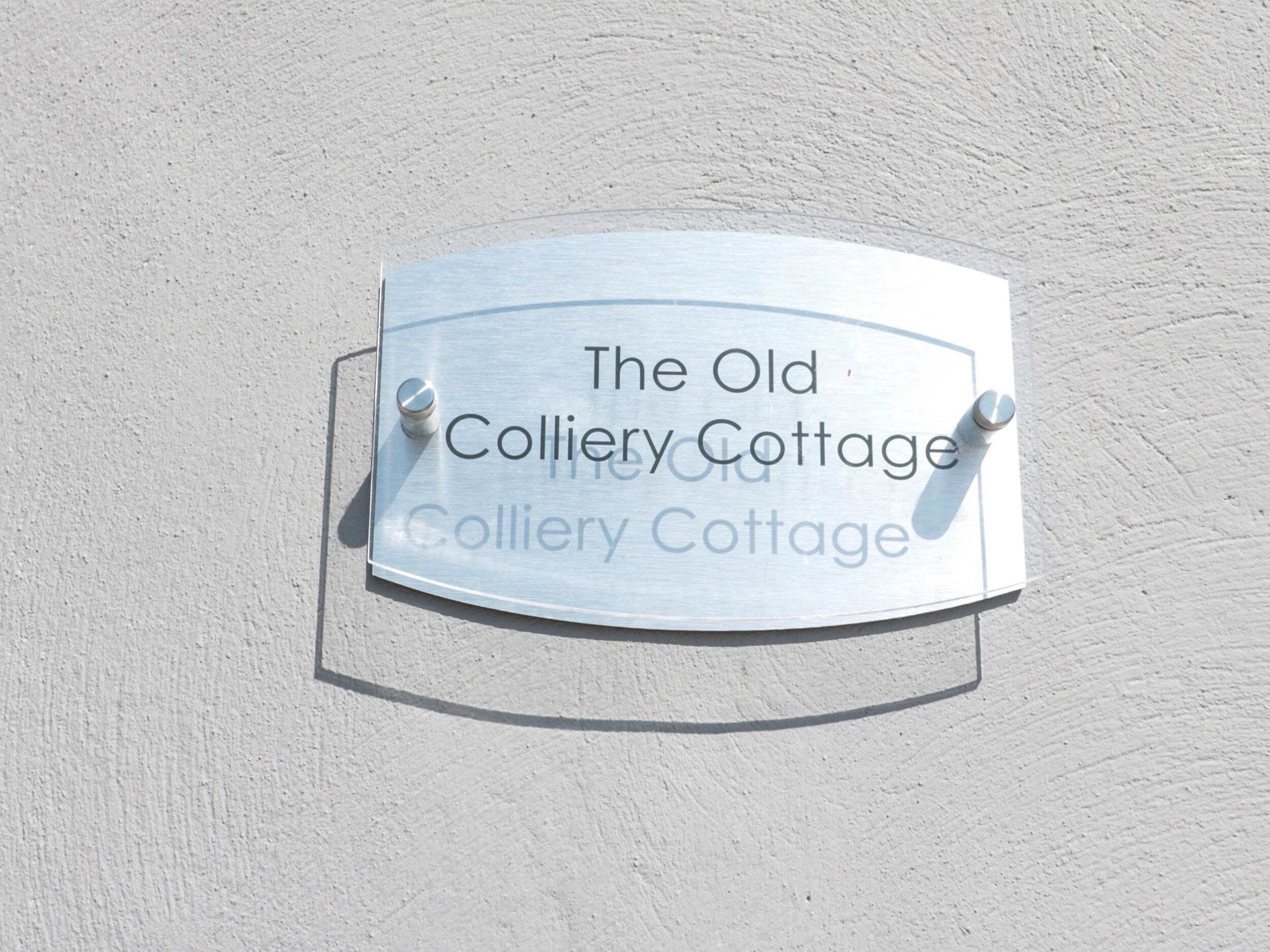 A metal sign with the text "The Old Colliery Cottage" mounted on a wall.