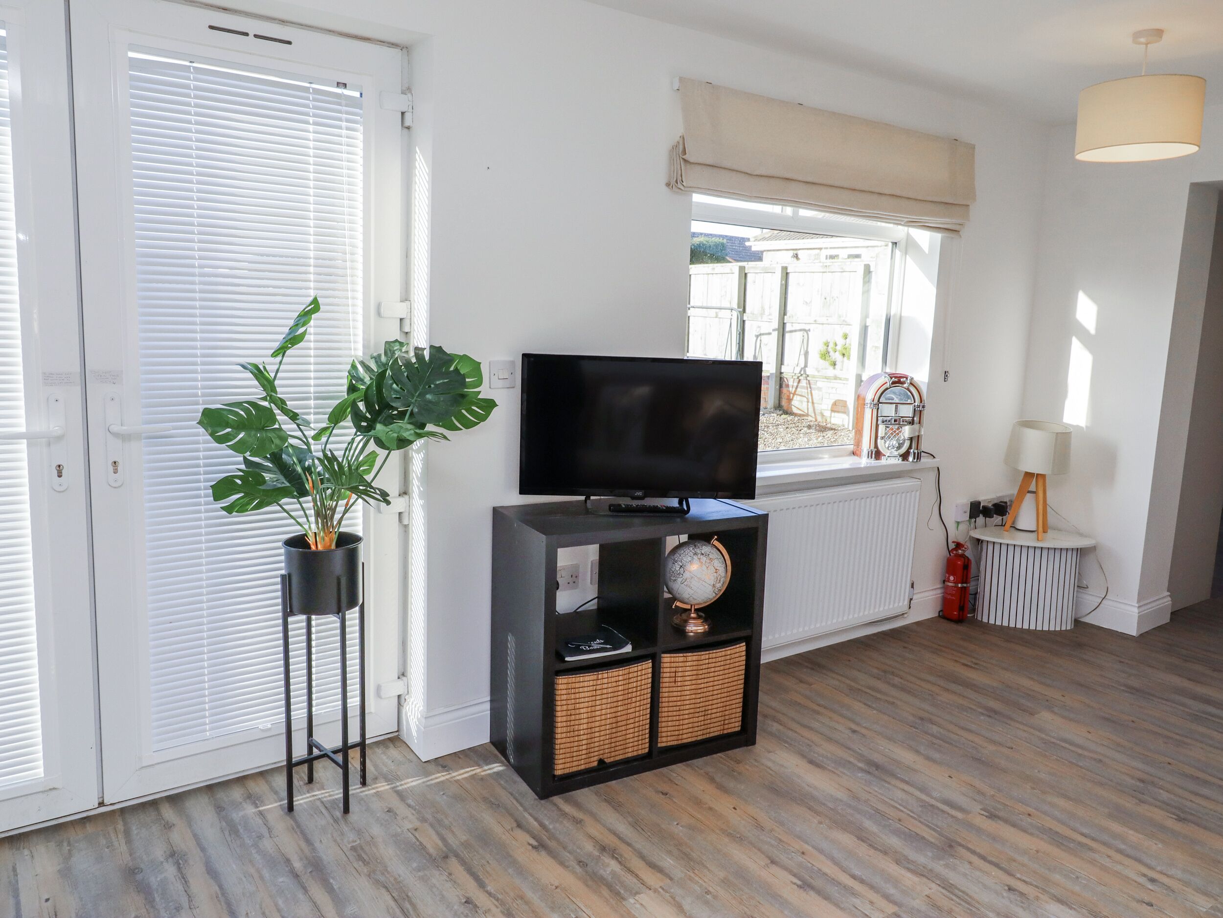Una sala de estar con un televisor sobre un soporte negro, una planta en maceta, un globo terráqueo y un radiador.