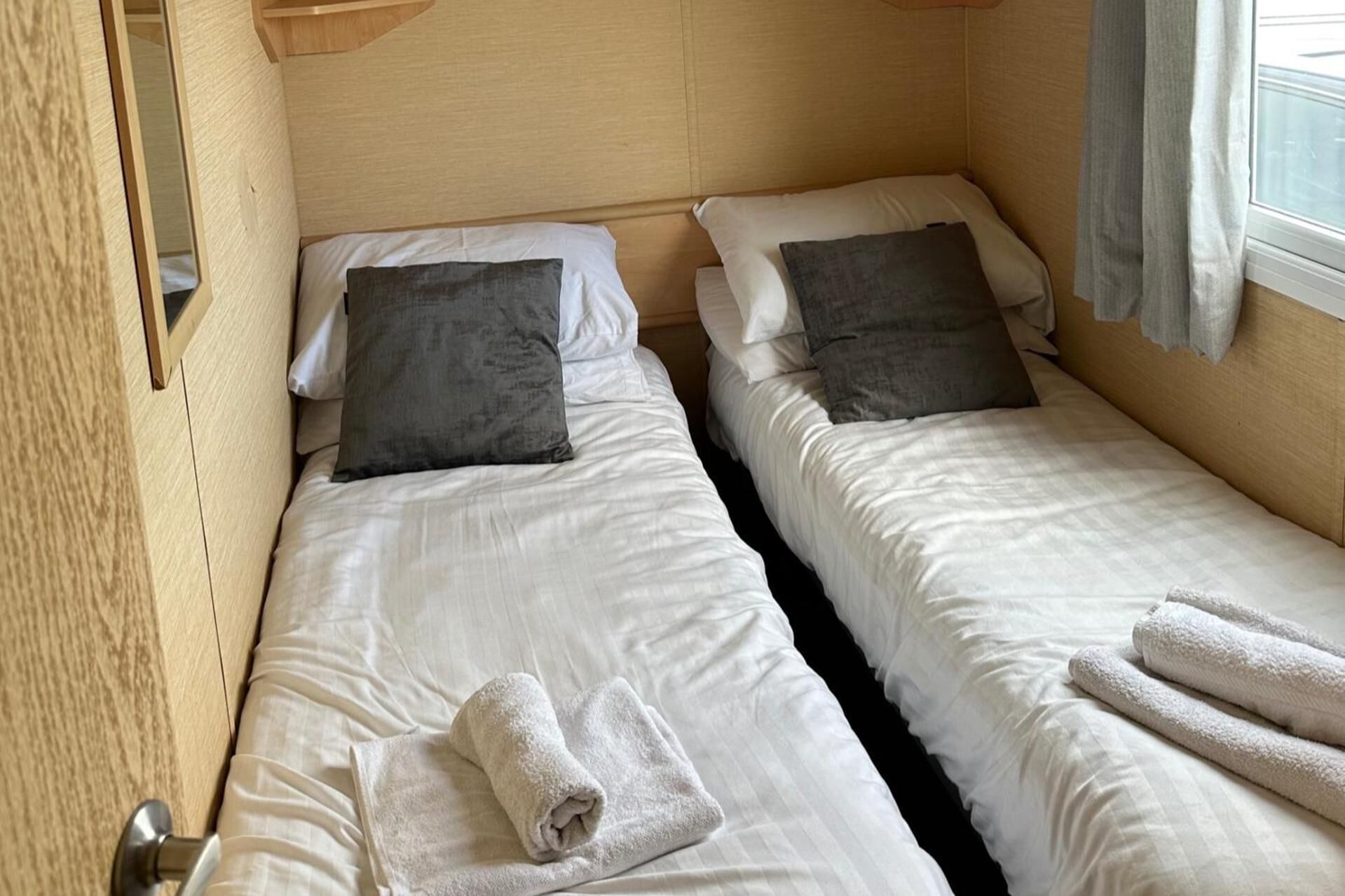 A compact bedroom with two single beds, each with a pillow and a rolled towel.