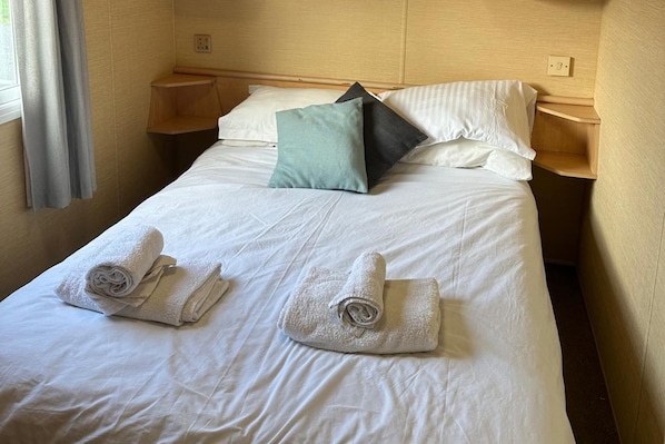 A neatly made bed with white linens, two rolled towels, and a teal pillow.