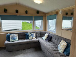 A cozy living area with a grey sectional sofa, multiple cushions, and potted plants on a wooden shelf.