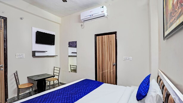 A hotel room with a bed, a desk, a chair, a TV mounted on the wall, and an air conditioning unit. - Hotel FNG Metro View (Noida)