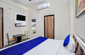 A hotel room with a bed, a desk, a chair, a TV mounted on the wall, and an air conditioning unit. - Hotel FNG Metro View (Noida)