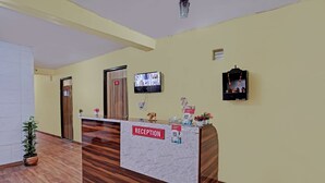 A reception desk with a "RECEPTION" sign, a mounted TV, and a small statue. - Hotel FNG Metro View (Noida)