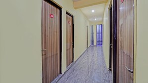 A hallway with wooden doors marked with room numbers, leading to a room with a window and a view. - Hotel FNG Metro View (Noida)