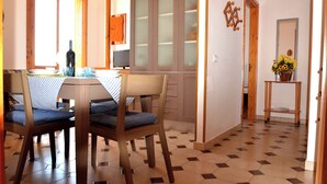 Un área de comedor con una mesa, sillas y un televisor. Hay un armario con puertas de cristal satinado y una puerta de madera con un número.