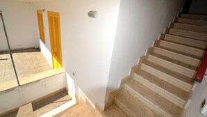 Una escalera de madera con escalones que conducen a un rellano, una pared blanca y una puerta amarilla.