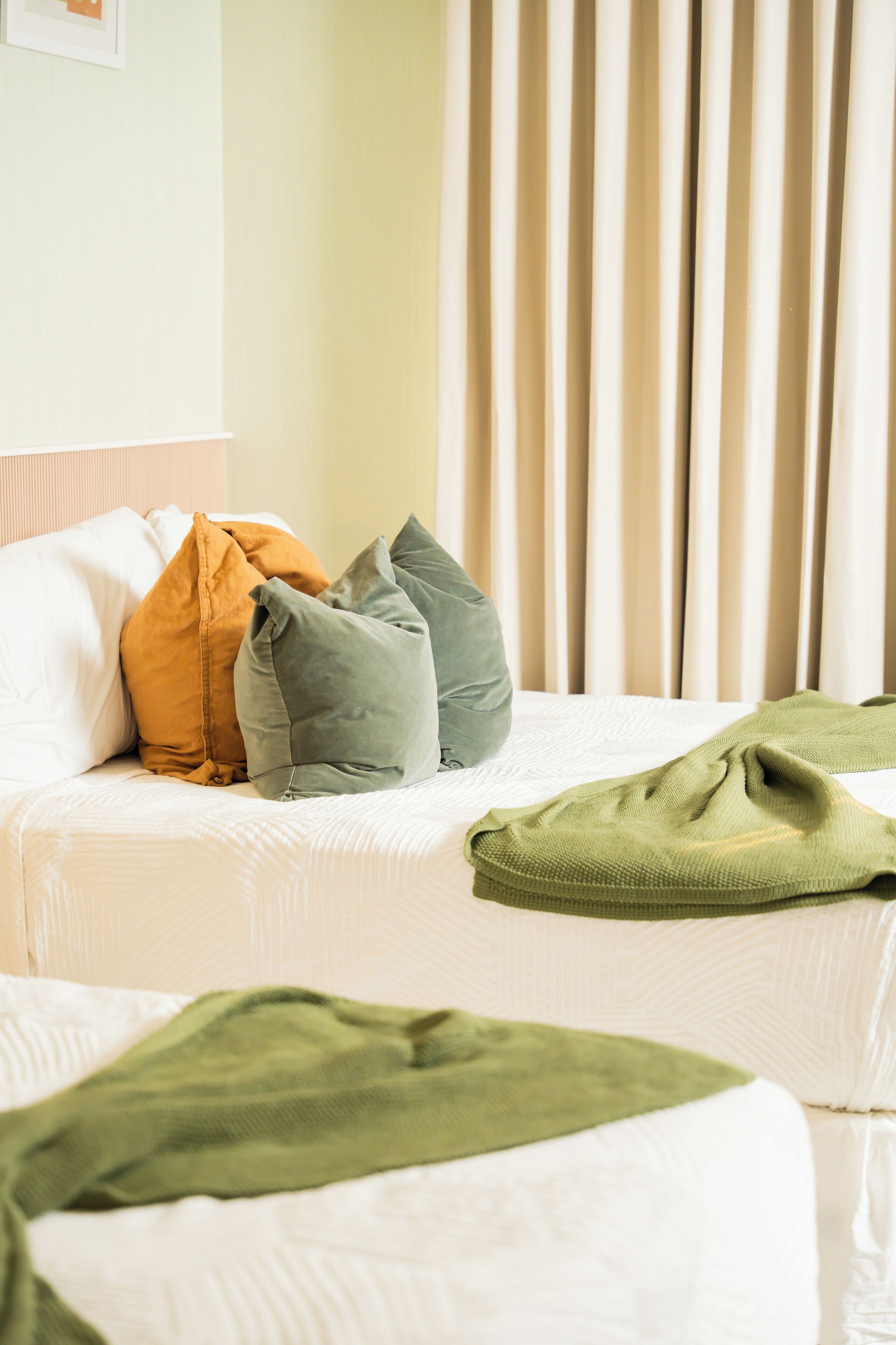 A hotel room with two beds, each with a white mattress and multiple pillows in various colors.