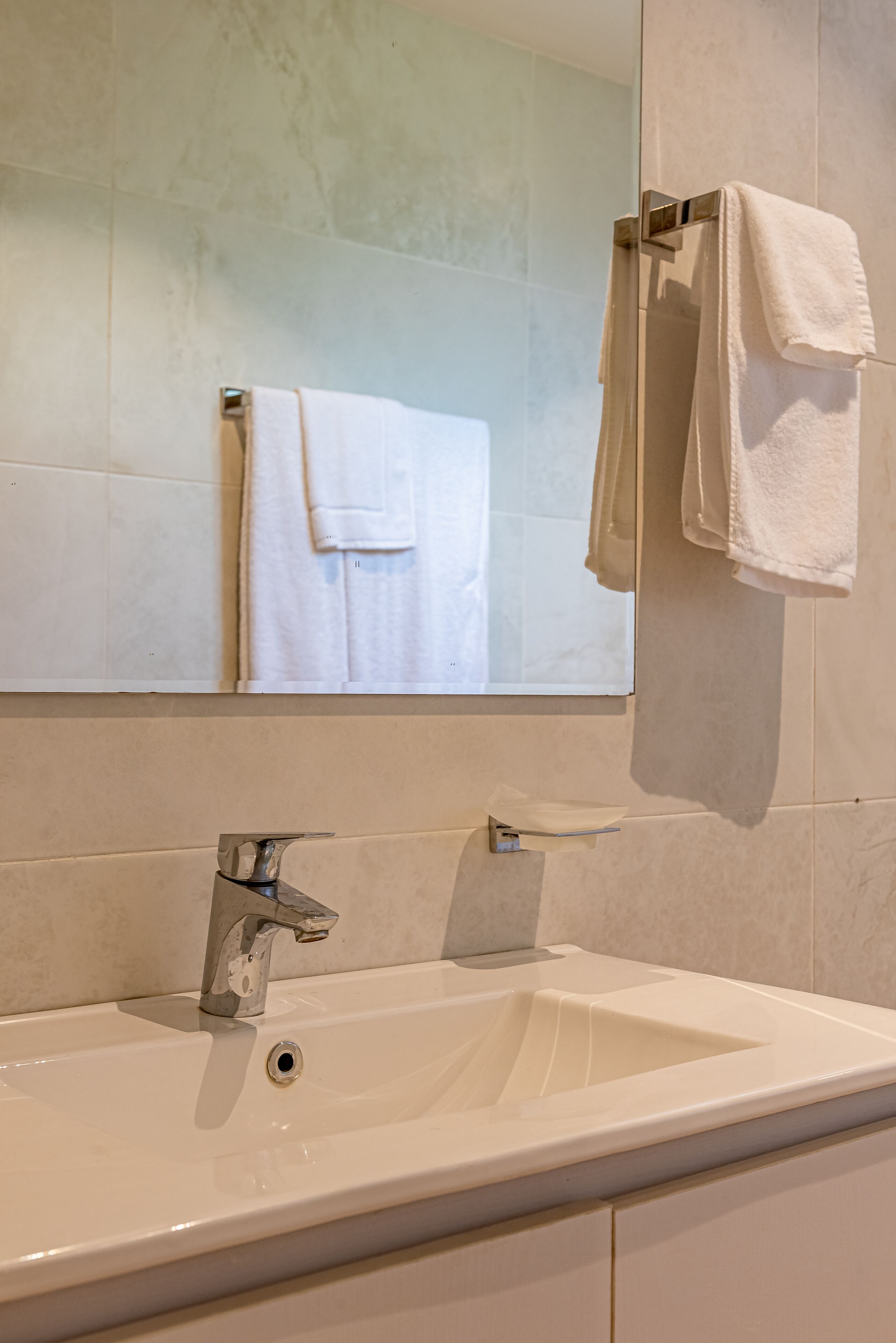 A bathroom with a white sink, a mirror, and a towel rack with two white towels.