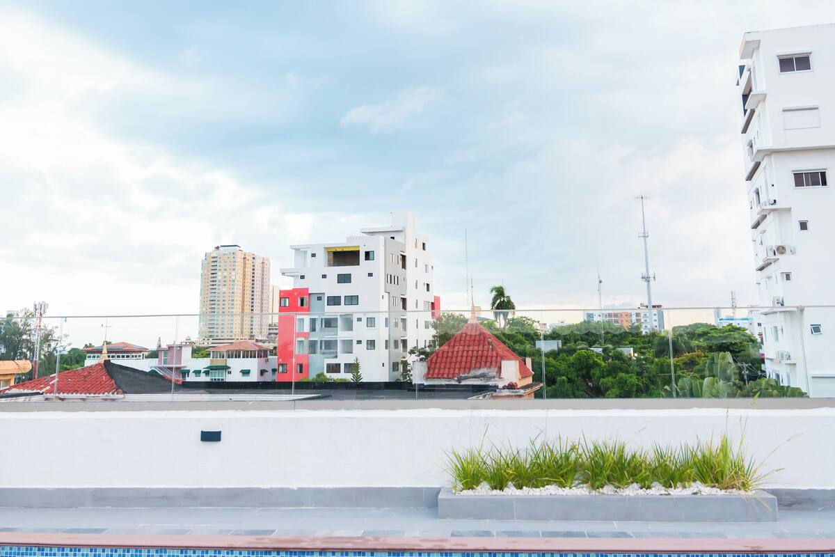 A swimming pool with a tiled edge, surrounded by a white building with a red roof and a white building with balconies.