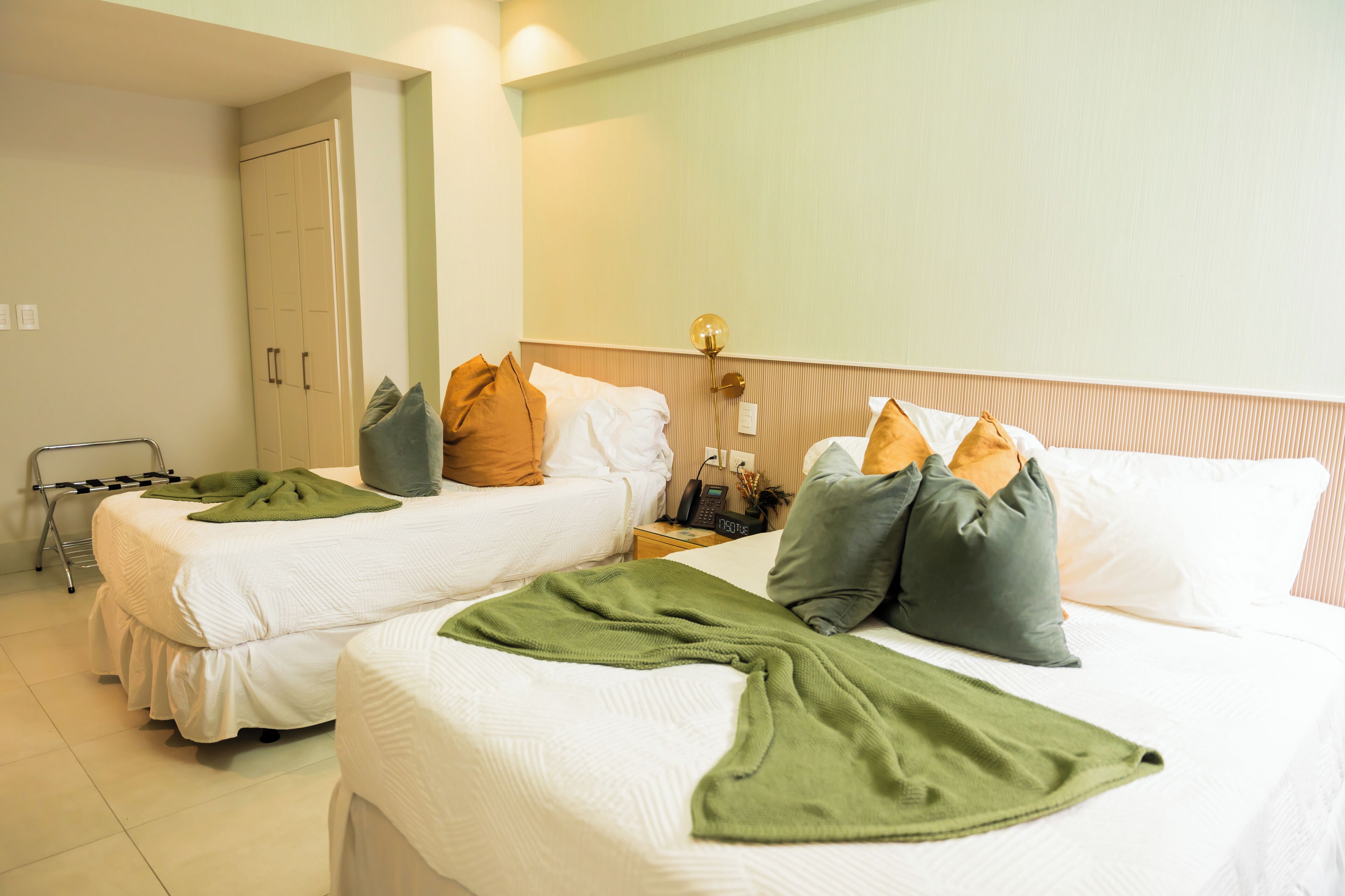Una habitación de hotel con dos camas individuales, una mesita de noche con lámpara y un armario.
