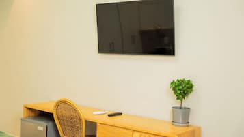 Une pièce comprenant un lit, un bureau avec une chaise, un téléviseur fixé au mur et une plante en pot.