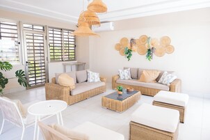 Un salón amplio con muebles de mimbre, una mesa de centro blanca y un ventanal con vistas.