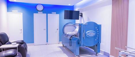 Et røntgenrum med en CT-scanner, hvilestole og et ur på væggen.