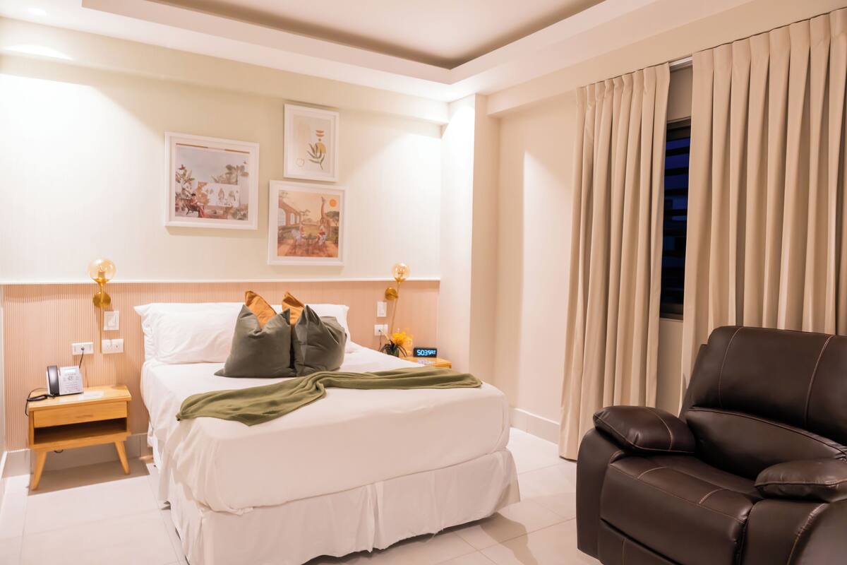 A hotel room with a bed, a nightstand, a lamp, a chair, and curtains.